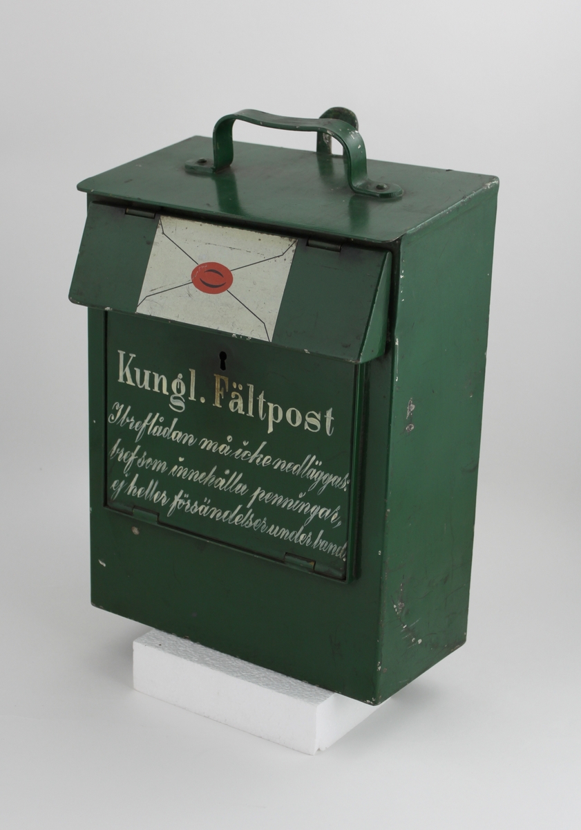 Brevlåda, med fronttömning, på klaffen över brevinkastet finns ett målat sigillförsett kuvert. På brevlådans tak finns ett handtag.