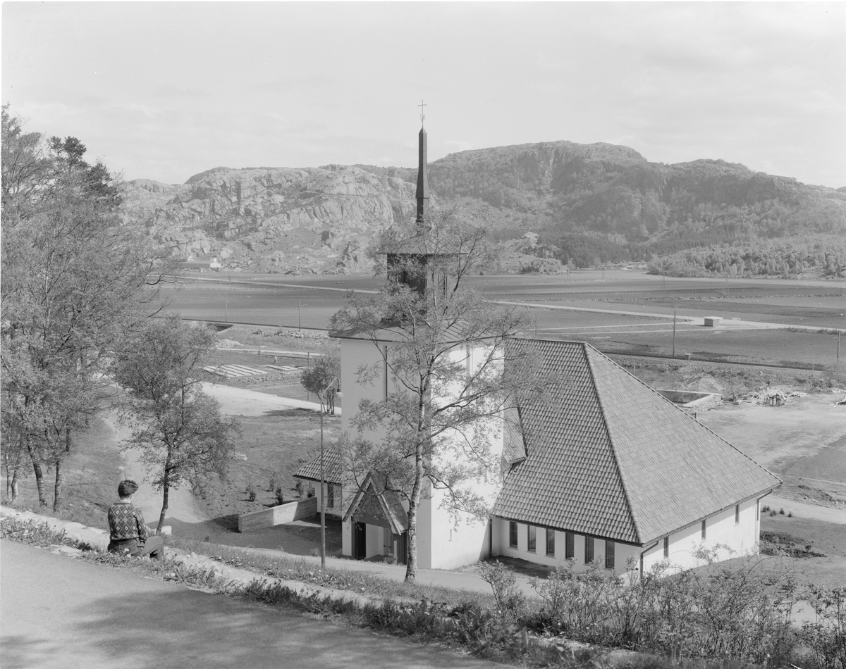 En person sitter i bakken ovenfor Bakkebø kirke i Egersund og ser utover.