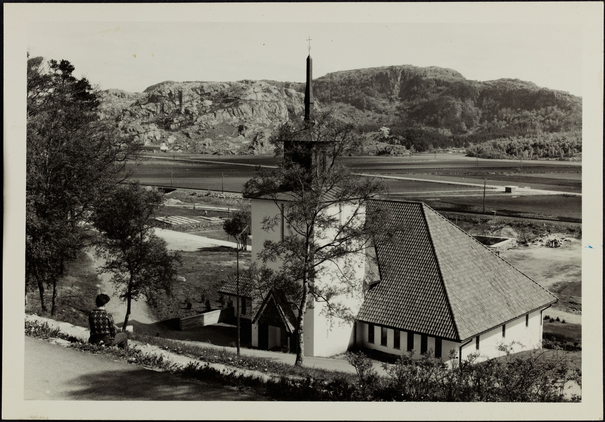 En person sitter i bakken ovenfor Bakkebø kirke i Egersund og ser utover.