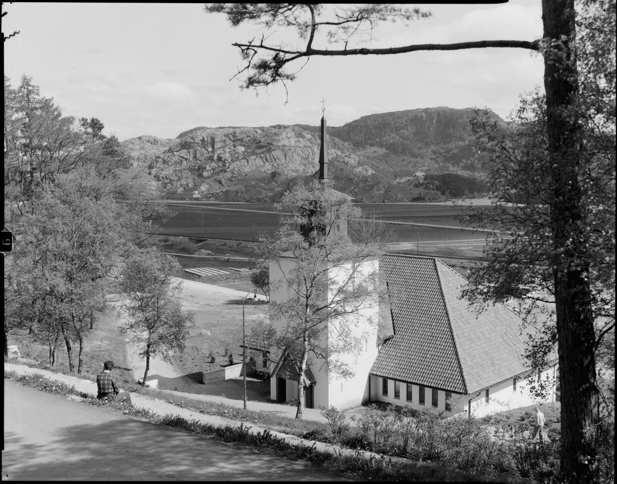 En person sitter i bakken ovenfor Bakkebø kirke i Egersund og ser utover.