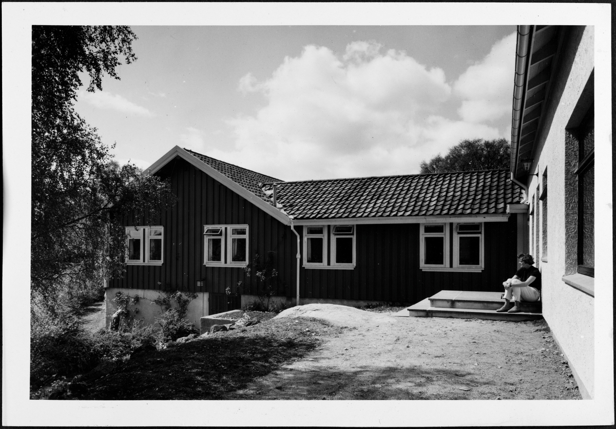 Bærumsgården på Bakkebø hjem og arbeidsskole. En kvinne sitter på trappeoppgangen.