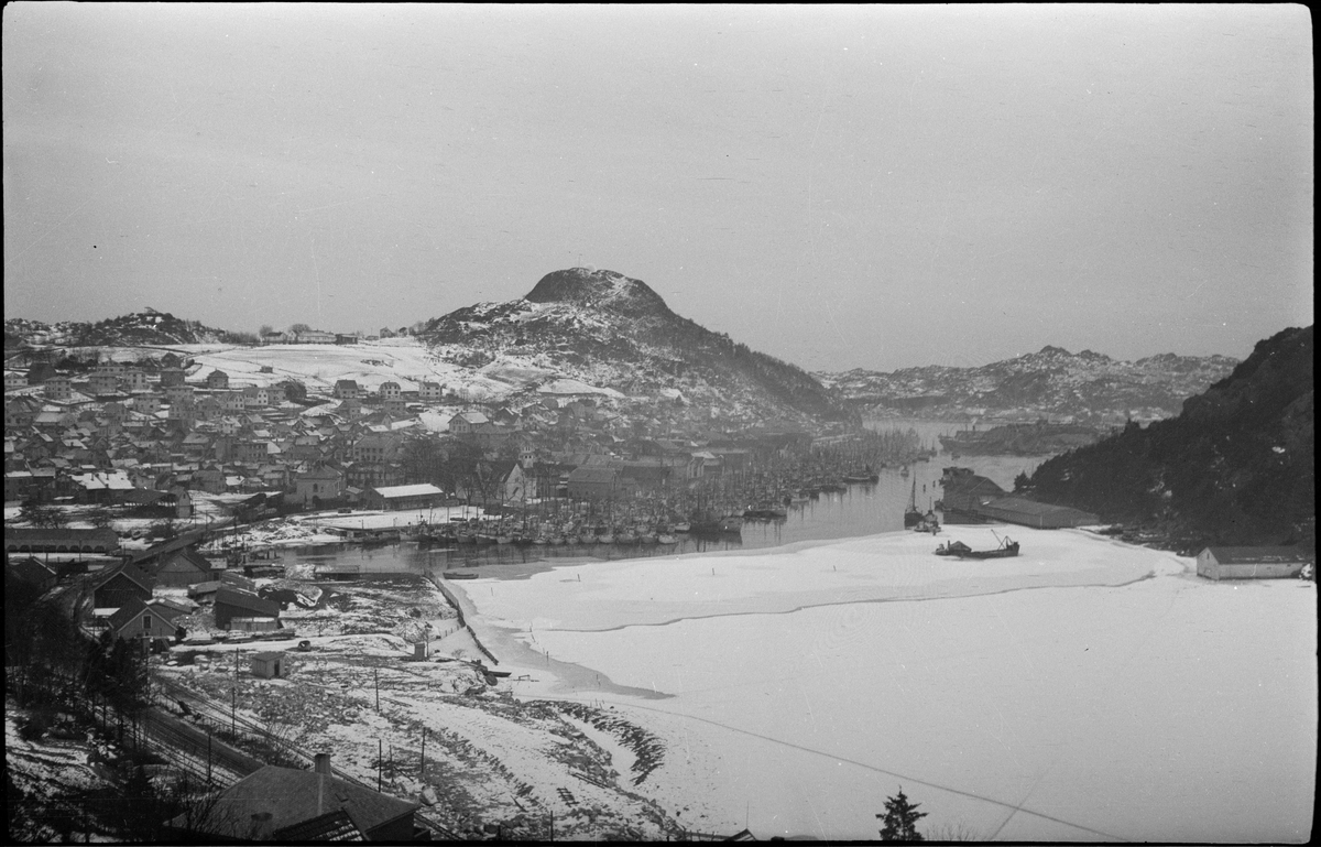 Utsikt over Vågen og Egersund en vinterdag. Det fiskeflåten ligger til kai og den innerste delen av Vågen er islagt. På bilde nr. 3 ser to menn ut over byen.