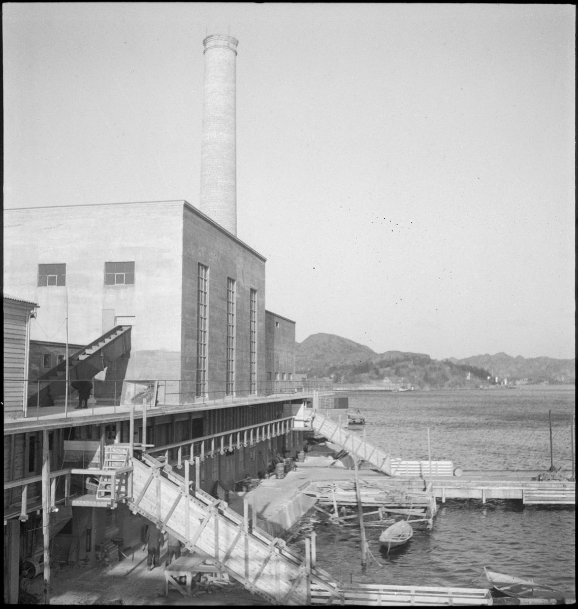 Sildoljefabrikken SILFAS på Grønehaugen i Eigersund rundt ferdigstillelse. Det er bilder av fabrikken, sildekummene og produksjonslinjene, samt en maskin.
