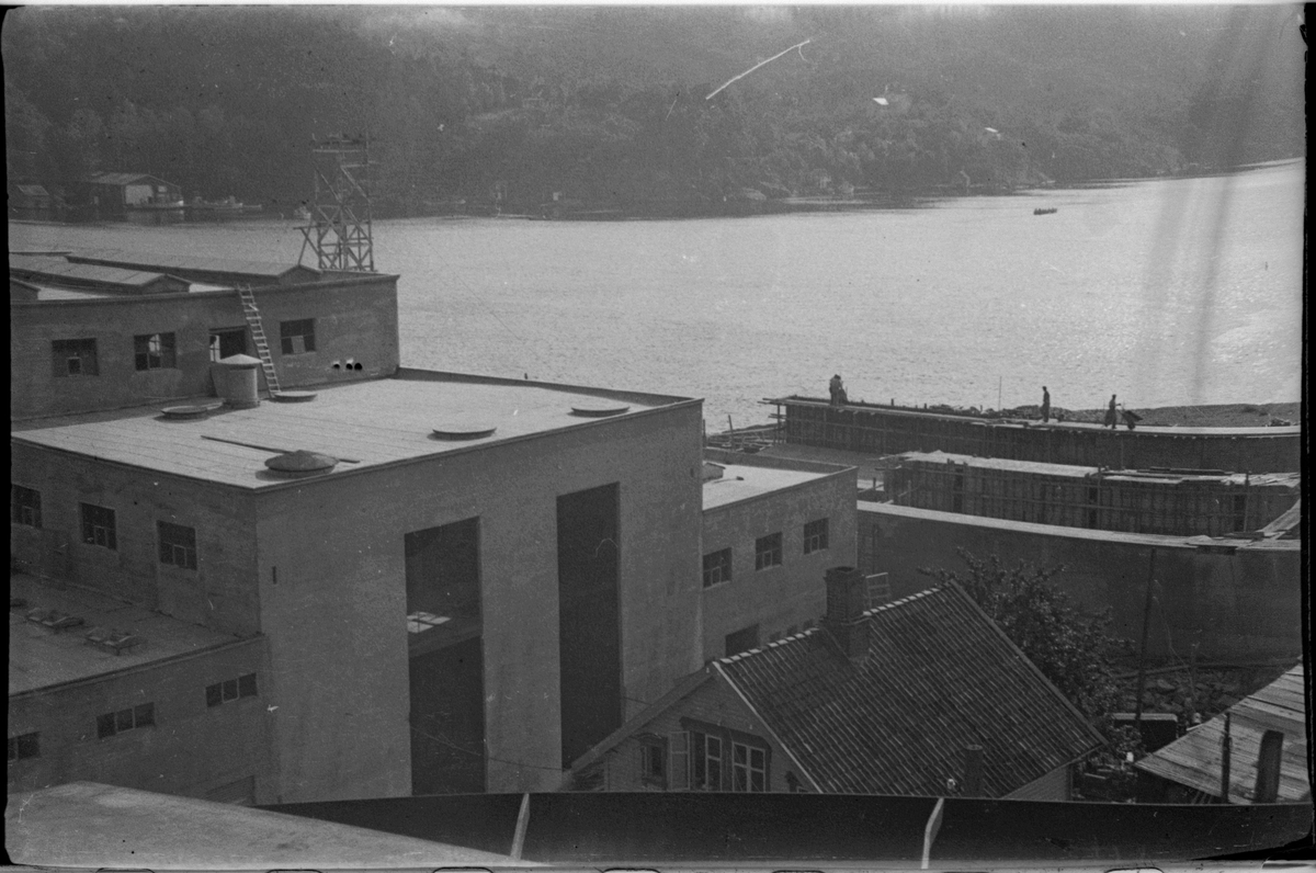 Sildoljefabrikken SILFAS på Grønehaugen i Eigersund rundt ferdigstillelse. Det er bilder av fabrikken, sildekummene og produksjonslinjene, samt en maskin.