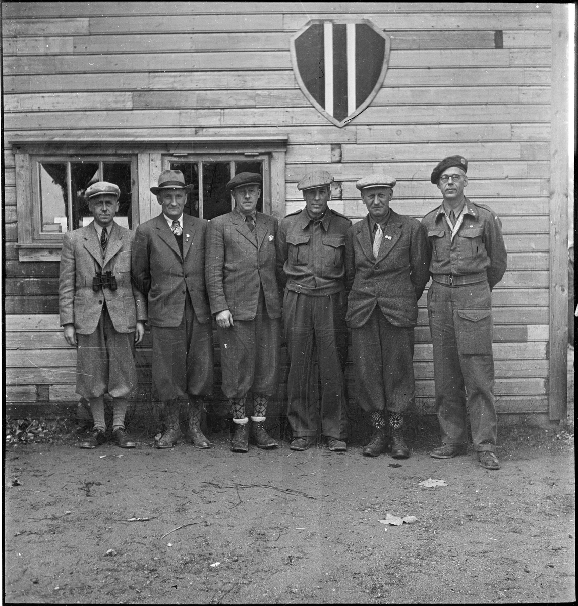 Seks menn står under logoen til Egersund skytterlag på Nyeveien. To har på militær- eller heimevernsuniform.