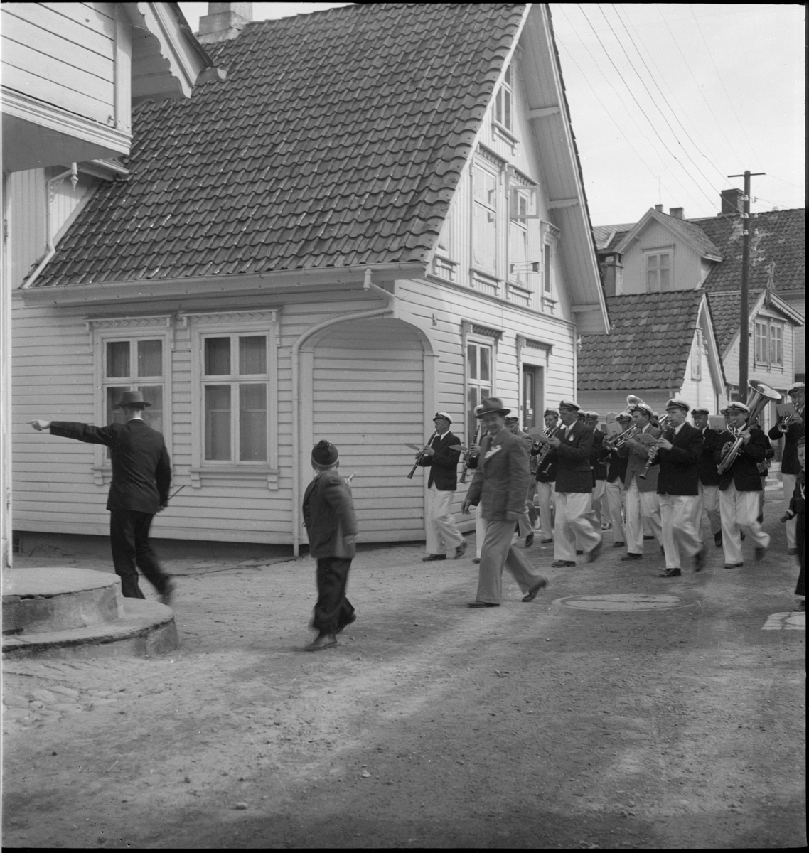 Folketog på 17. mai. Flere korps og barn går langs Vågen og igjennom sentrum av Egersund. Mange har kommet for å se toget.