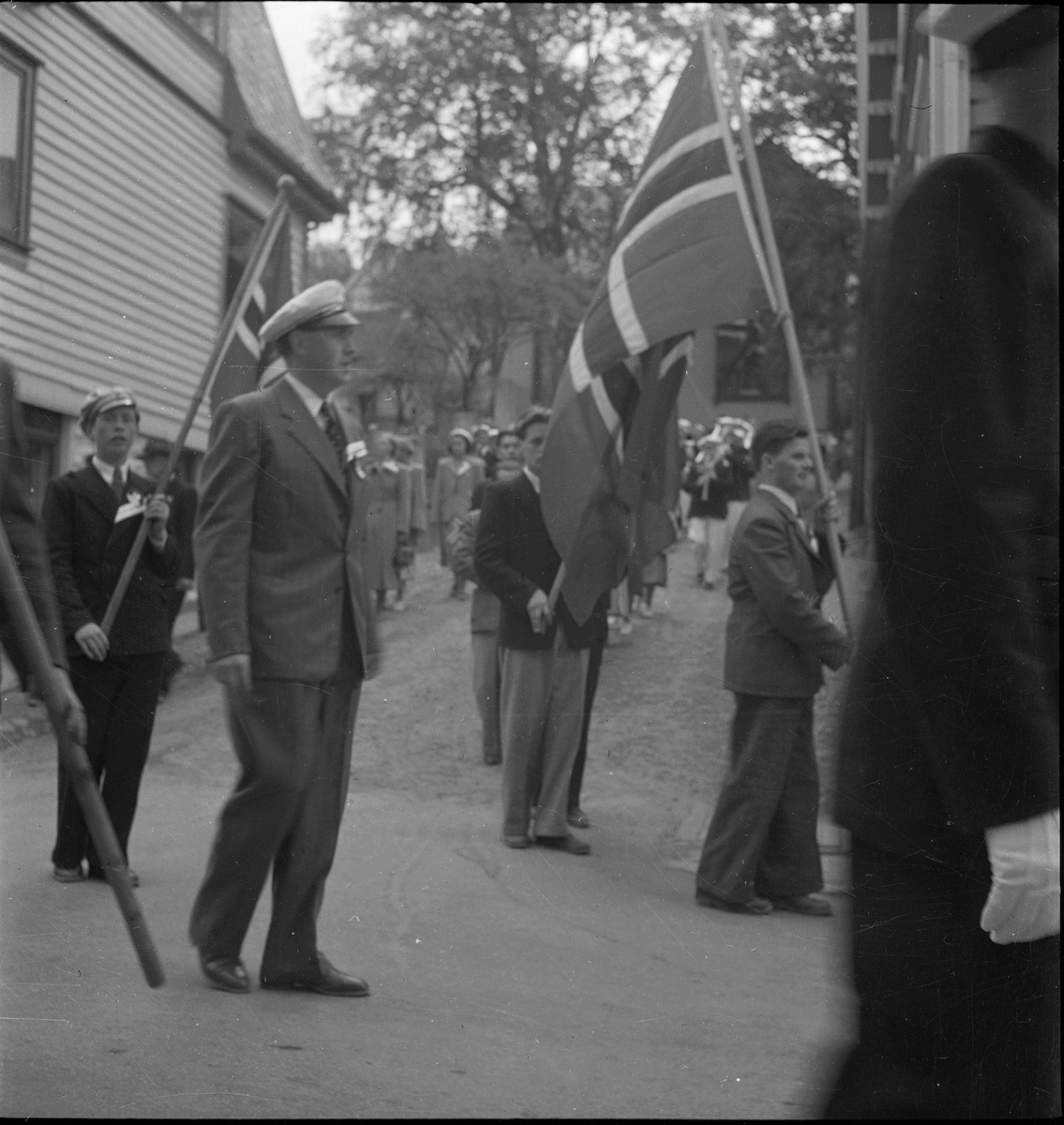 Folketog på 17. mai. Flere korps og barn går langs Vågen og igjennom sentrum av Egersund. Mange har kommet for å se toget.