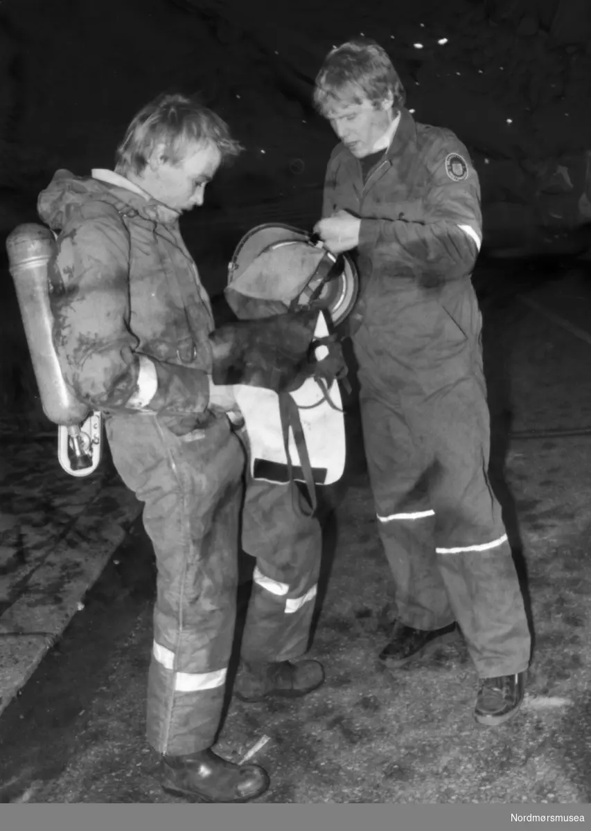 To brannmenn. Fotografert i forbindelse med brann ved Sverdrups bokhandel i Kaibakken på Kirkelandet i Kristiansund. Nyttårsaften 1987. Bildet er fra avisa Tidens Krav sitt arkiv i tidsrommet 1970-1994. Nå i Nordmøre museums fotosamling.