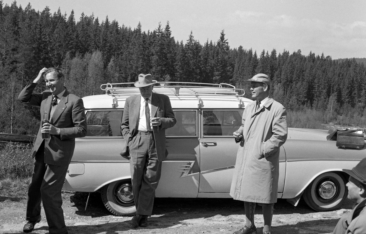 Fra Glomma fellesfløtingsforenings direksjonsbefaring i 1961. Direksjonen (styret) og lederne i organisasjonen besøkte 3., 4., 5., og 6. distrikt. Da dette fotografiet ble tatt hadde karene stanset og det ble servert dram. Bilen i bakgrunnen er en Ford Taunus 17 M stasjonsvogn, en modell fra 1958-1960.