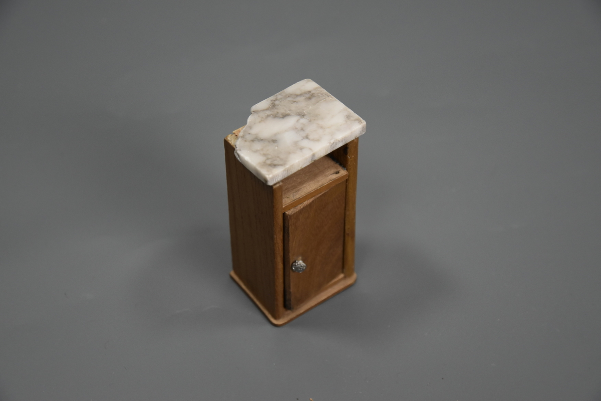 Vaskevannstol i toalettmøblement til dokkemøblement i treverk med steinplate. Plata er skadet. Dokkemøbler ble gitt til jenter til lek som forberedelse til voksenlivet.  