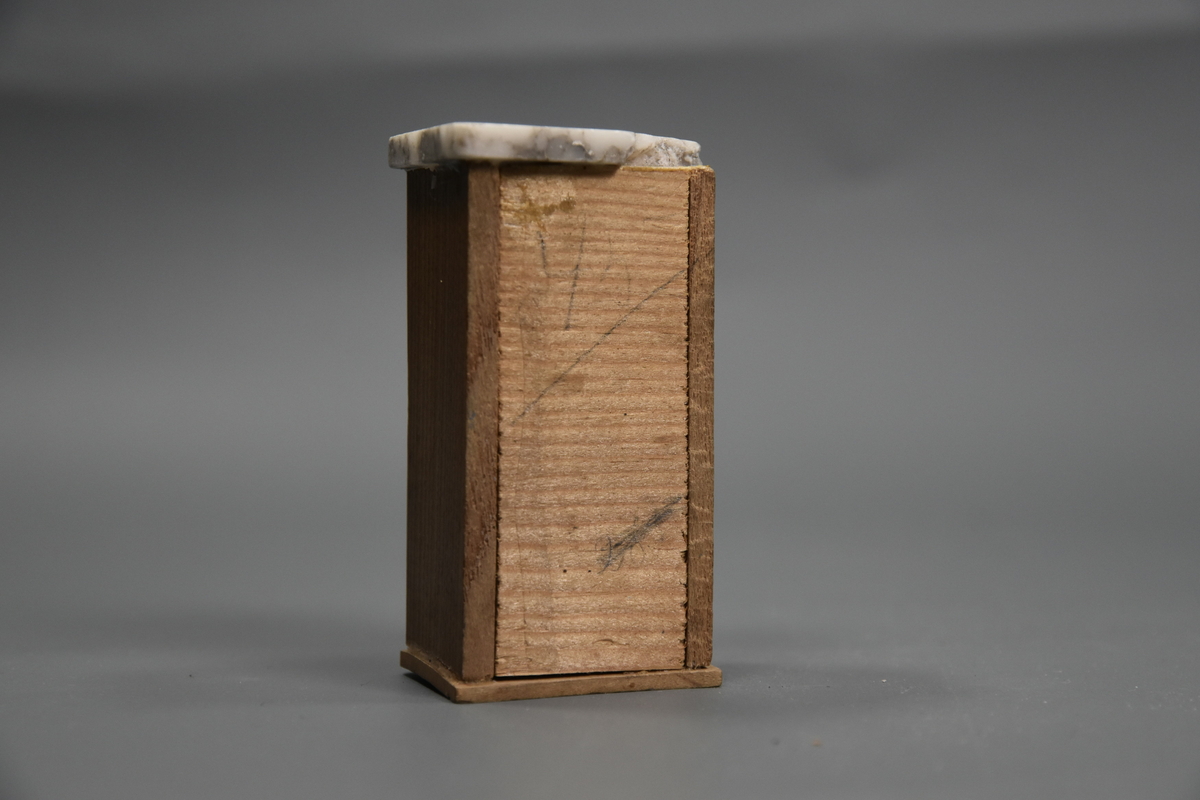 Vaskevannstol i toalettmøblement til dokkemøblement i treverk med steinplate. Plata er skadet. Dokkemøbler ble gitt til jenter til lek som forberedelse til voksenlivet.  