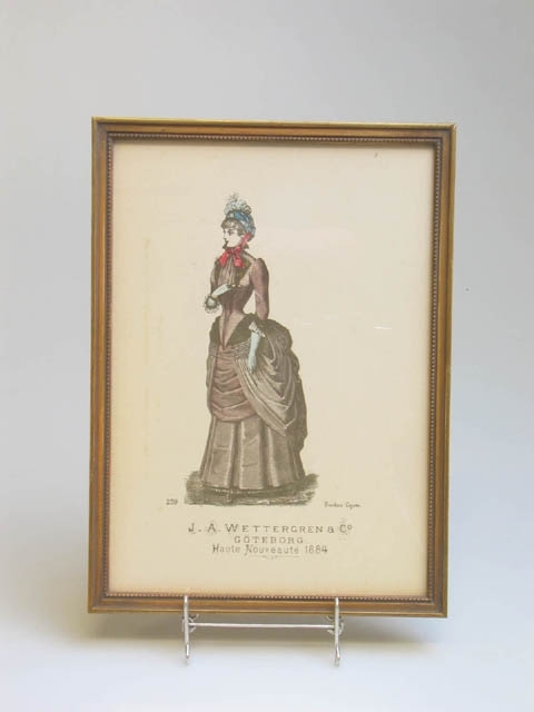 Två modeplanscher från J.A. Wettergren, Göteborg. Föreställer kvinnor i 1884 års mode av Gustav Lyon. Under namnet Wettergren står det "Haute Nouveauté 1884". Planscherna är inramade i guldmålade träramar. Klistermärke baktill med text "RAMBRÖDERNA GÖTEBORG".