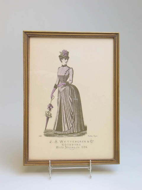 Två modeplanscher från J.A. Wettergren, Göteborg. Föreställer kvinnor i 1884 års mode av Gustav Lyon. Under namnet Wettergren står det "Haute Nouveauté 1884". Planscherna är inramade i guldmålade träramar. Klistermärke baktill med text "RAMBRÖDERNA GÖTEBORG".
