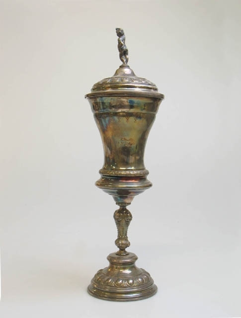 Två fotbollspokaler.
1) Pokal formad som en ölsejdel av förvilvrad mässing med nyrokokodekor. Lock med handtag. Delar av handtaget på sidan av sejdeln och handtaget på locket är av tenn. Text: "Fotboll Landskrona 19 24/4 03". Stämplar undertill: "F.W.Q.L.". Mått: H 27, Diam upptill 10,5, Diam nedtill 12,5 cm.
2) Pokal av förvilvrad mässing med nyrokokodekor. Lock med handtag i form av en pojke. Text: "Fotboll Wäsby 19 14/8 04". Mått: H 42, Diam upptill 12, Diam nedtill 11 cm.