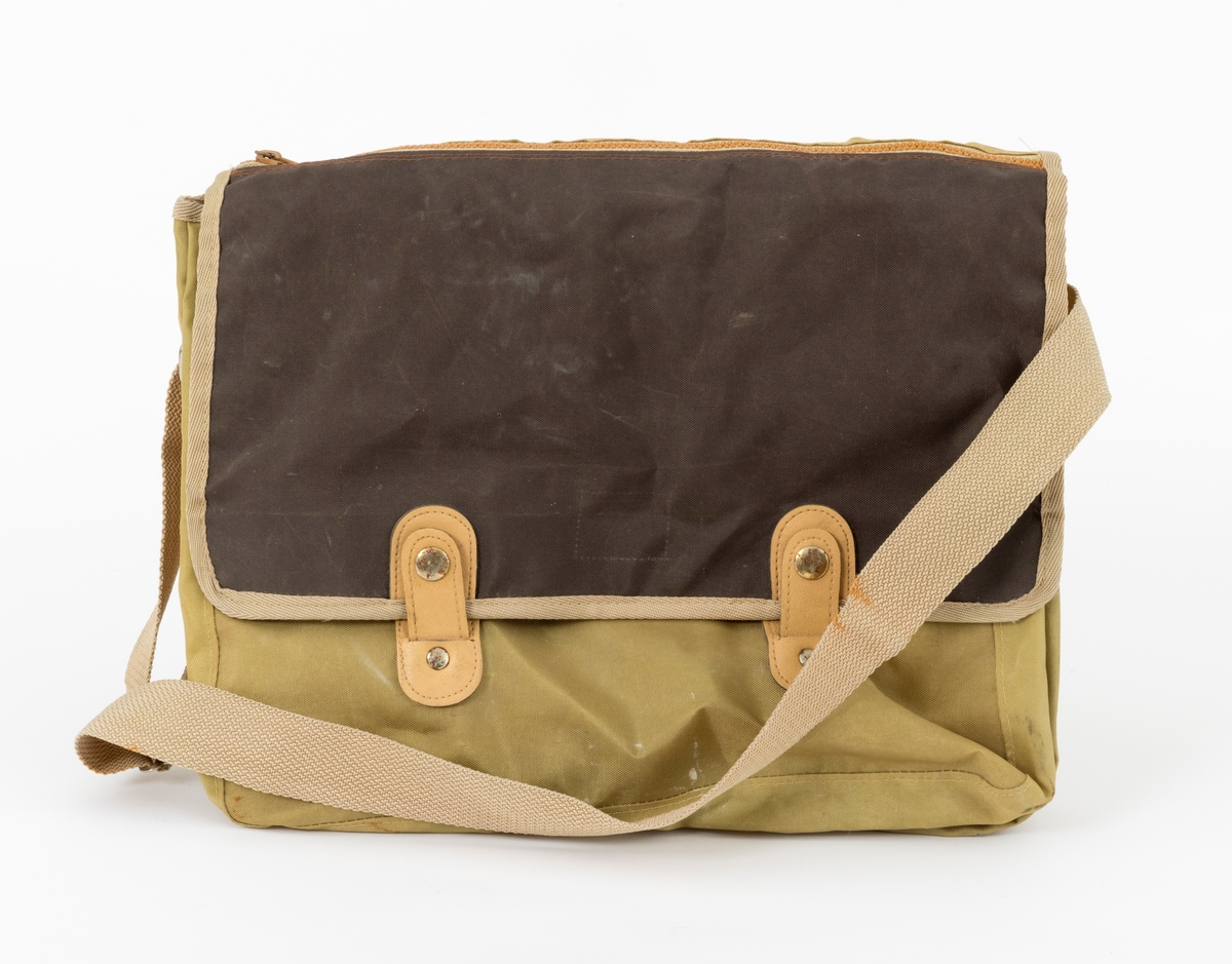 Veske med skulderreim brukt til å oppbevare utstyr under fiske. Veska er ei klaffeveske laget i grønt og brunt nylonstoff med detaljer i lyst kunstklær og metall. Den er kantet med beige bånd, samme farge som skulderreima. Veska består av et stort rom, i tillegg til to lommer, ei ytterlomme og ei lomme på utsiden av klaffen. Veska lukkes med to tykknapper. Lommene lukkes med glidelås.