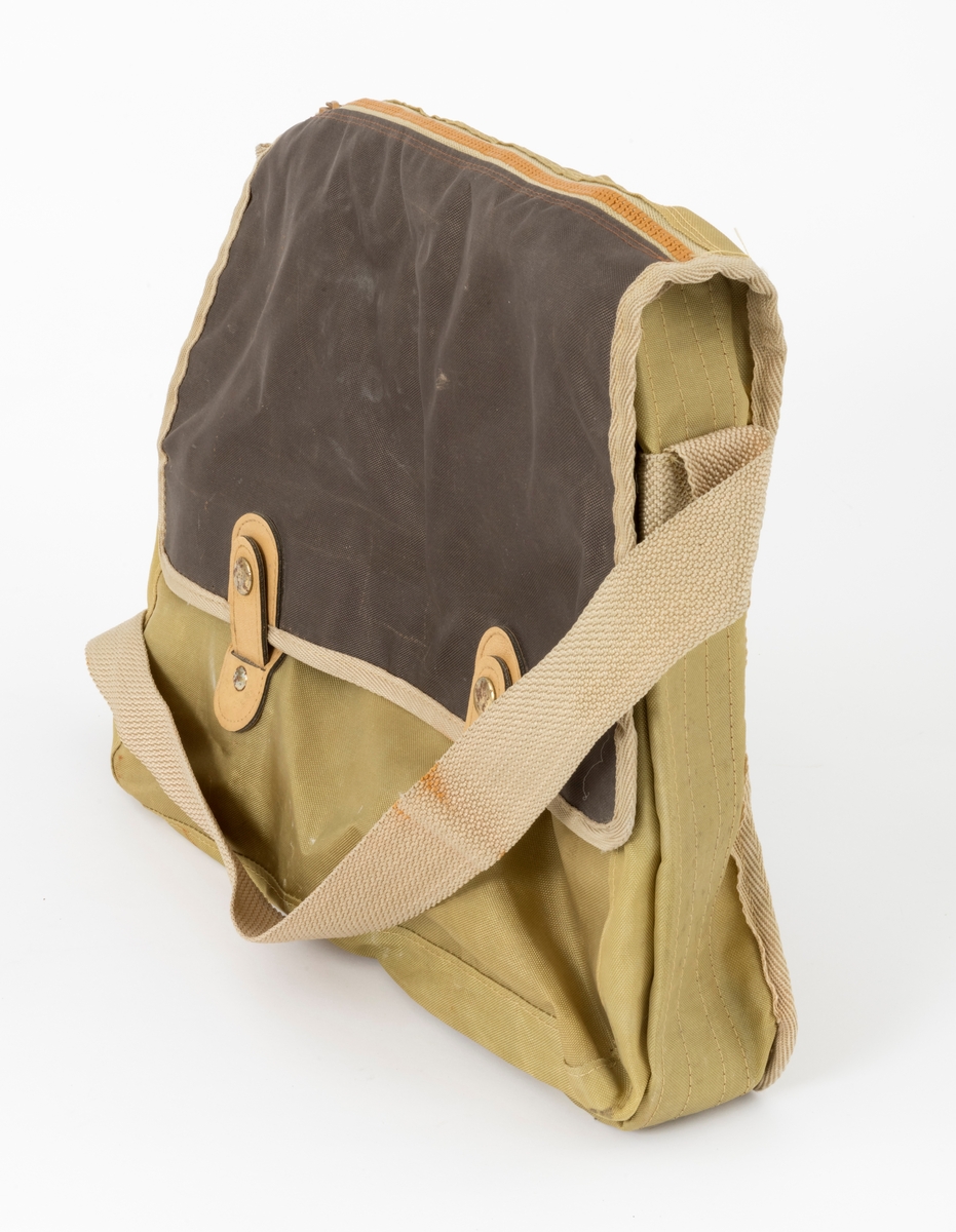 Veske med skulderreim brukt til å oppbevare utstyr under fiske. Veska er ei klaffeveske laget i grønt og brunt nylonstoff med detaljer i lyst kunstklær og metall. Den er kantet med beige bånd, samme farge som skulderreima. Veska består av et stort rom, i tillegg til to lommer, ei ytterlomme og ei lomme på utsiden av klaffen. Veska lukkes med to tykknapper. Lommene lukkes med glidelås.