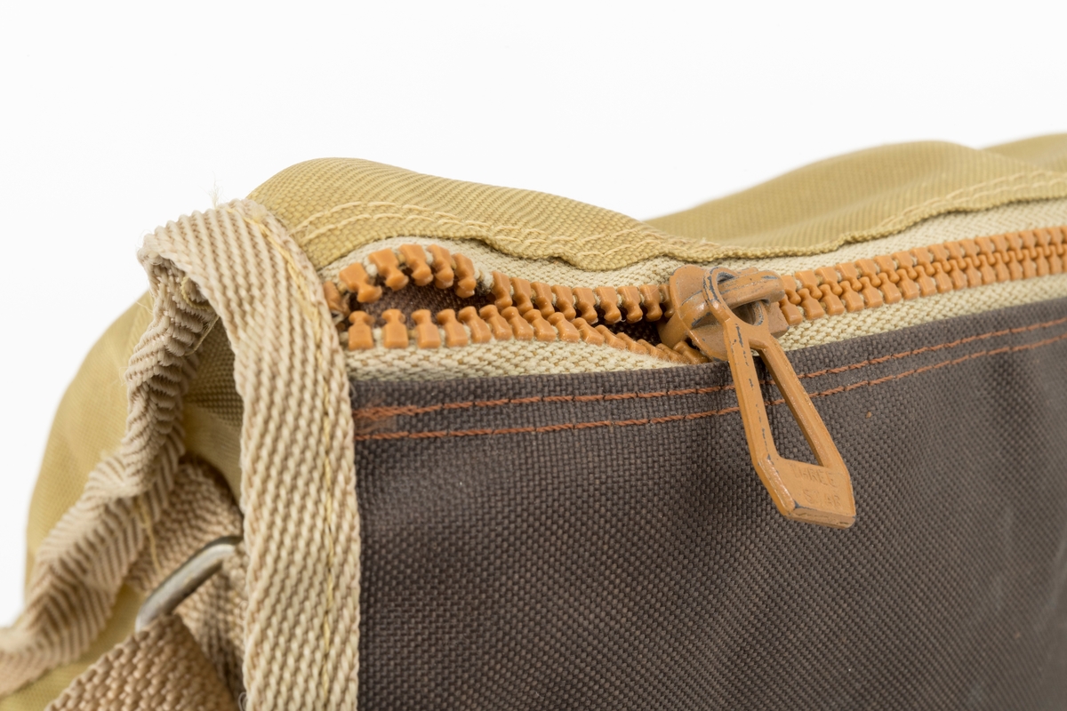 Veske med skulderreim brukt til å oppbevare utstyr under fiske. Veska er ei klaffeveske laget i grønt og brunt nylonstoff med detaljer i lyst kunstklær og metall. Den er kantet med beige bånd, samme farge som skulderreima. Veska består av et stort rom, i tillegg til to lommer, ei ytterlomme og ei lomme på utsiden av klaffen. Veska lukkes med to tykknapper. Lommene lukkes med glidelås.