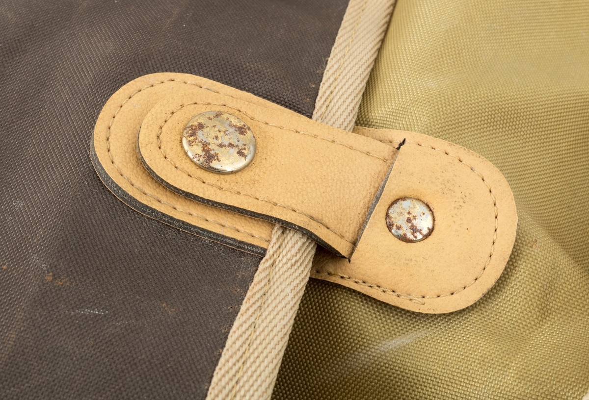 Veske med skulderreim brukt til å oppbevare utstyr under fiske. Veska er ei klaffeveske laget i grønt og brunt nylonstoff med detaljer i lyst kunstklær og metall. Den er kantet med beige bånd, samme farge som skulderreima. Veska består av et stort rom, i tillegg til to lommer, ei ytterlomme og ei lomme på utsiden av klaffen. Veska lukkes med to tykknapper. Lommene lukkes med glidelås.