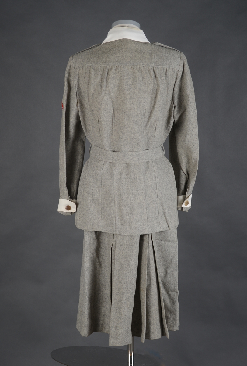 Lotteuniform består av jakke, skjørt og belte. Enkeltknept uniforms jakke med 4 utenpåsydde lommer med motfold og klaffer som lukkes med knapp og knapphull. Jakken lukkes med 1 trykk-knapp, 5 knapper og knapphull. 2 innsnitt i livet og 1 innsnitt fra skulder ned til bysten på hvert framstykke. Bakstykket har 4 innsnitt fra overkant av livlinjen og ned til nedre kant av jakken. Bærestykke øverst på ryggen. Ryggstykket er svakt rynket til bærestykket. Skulderstropper som festes med knapp og knapphull. Lange ermer med liten splitt og mansjett. Ermene er lagt i legg mot mansjettene. Jakken har skulderputer og innlegg under ermhulen.  Øverst på venstre erme er det sydd på 3 merker. Det øverste merket er av draktstoffet med tekst: Trondheim. Under det er det et rektangulært merke. Nederst et rundt merke, NLF merke. Løse hvite mansjetter på erme og løs krage rundt halsen. Kragen er sydd fast for hånd med lange sting. Jakken er lagt opp for hånd. Jakken har belte med spenne i livet og 2 beltestropper som er festet i sidene. På beltet er det to merker, 1 rundt sølvfarget festet med nål og et merke som er sydd fast.
Skjørtet har 2 motfolder foran og 2 bak. Linning i livet og åpning i venstre side som lukkes med metallglidelås, knapp og knapphull. Skjørtet er lagt opp for hånd. Drakten er uforet. Merkelapp langs glidelåset med tekst. 
Alle knapper på uniformen er merket NLF.