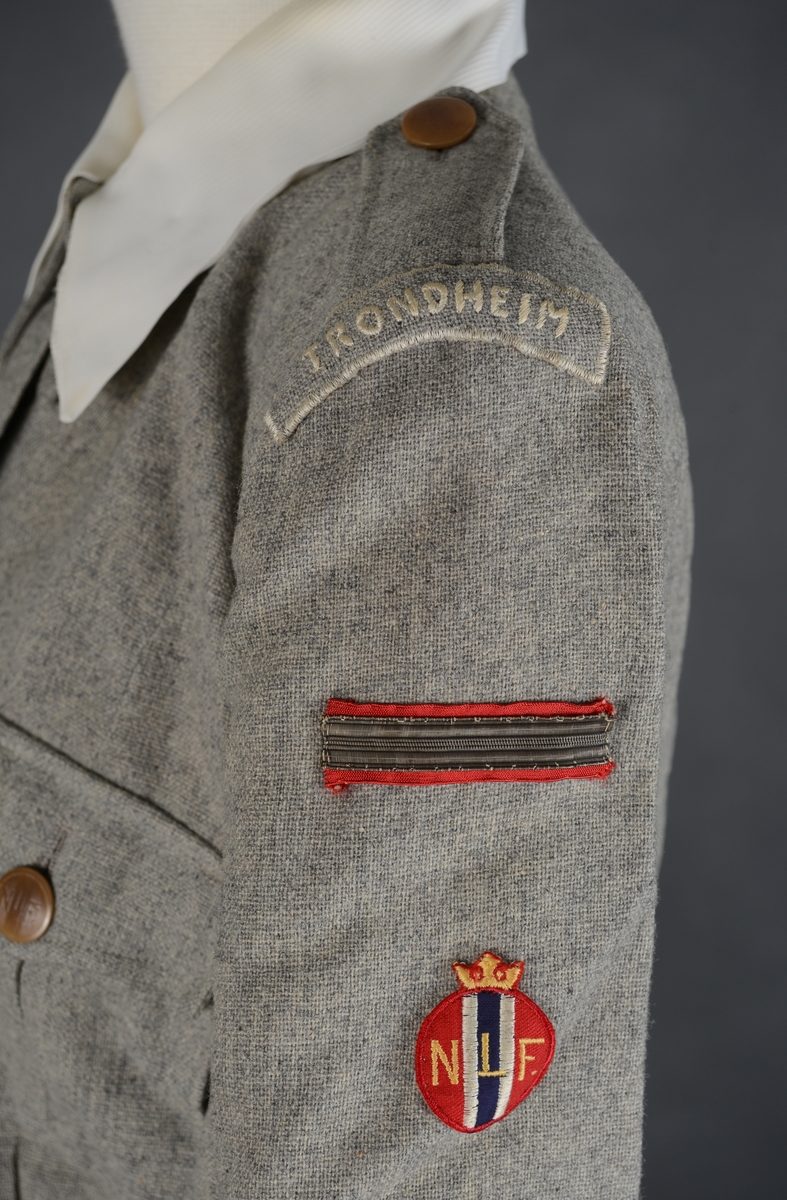 Lotteuniform består av jakke, skjørt og belte. Enkeltknept uniforms jakke med 4 utenpåsydde lommer med motfold og klaffer som lukkes med knapp og knapphull. Jakken lukkes med 1 trykk-knapp, 5 knapper og knapphull. 2 innsnitt i livet og 1 innsnitt fra skulder ned til bysten på hvert framstykke. Bakstykket har 4 innsnitt fra overkant av livlinjen og ned til nedre kant av jakken. Bærestykke øverst på ryggen. Ryggstykket er svakt rynket til bærestykket. Skulderstropper som festes med knapp og knapphull. Lange ermer med liten splitt og mansjett. Ermene er lagt i legg mot mansjettene. Jakken har skulderputer og innlegg under ermhulen.  Øverst på venstre erme er det sydd på 3 merker. Det øverste merket er av draktstoffet med tekst: Trondheim. Under det er det et rektangulært merke. Nederst et rundt merke, NLF merke. Løse hvite mansjetter på erme og løs krage rundt halsen. Kragen er sydd fast for hånd med lange sting. Jakken er lagt opp for hånd. Jakken har belte med spenne i livet og 2 beltestropper som er festet i sidene. På beltet er det to merker, 1 rundt sølvfarget festet med nål og et merke som er sydd fast.
Skjørtet har 2 motfolder foran og 2 bak. Linning i livet og åpning i venstre side som lukkes med metallglidelås, knapp og knapphull. Skjørtet er lagt opp for hånd. Drakten er uforet. Merkelapp langs glidelåset med tekst. 
Alle knapper på uniformen er merket NLF.