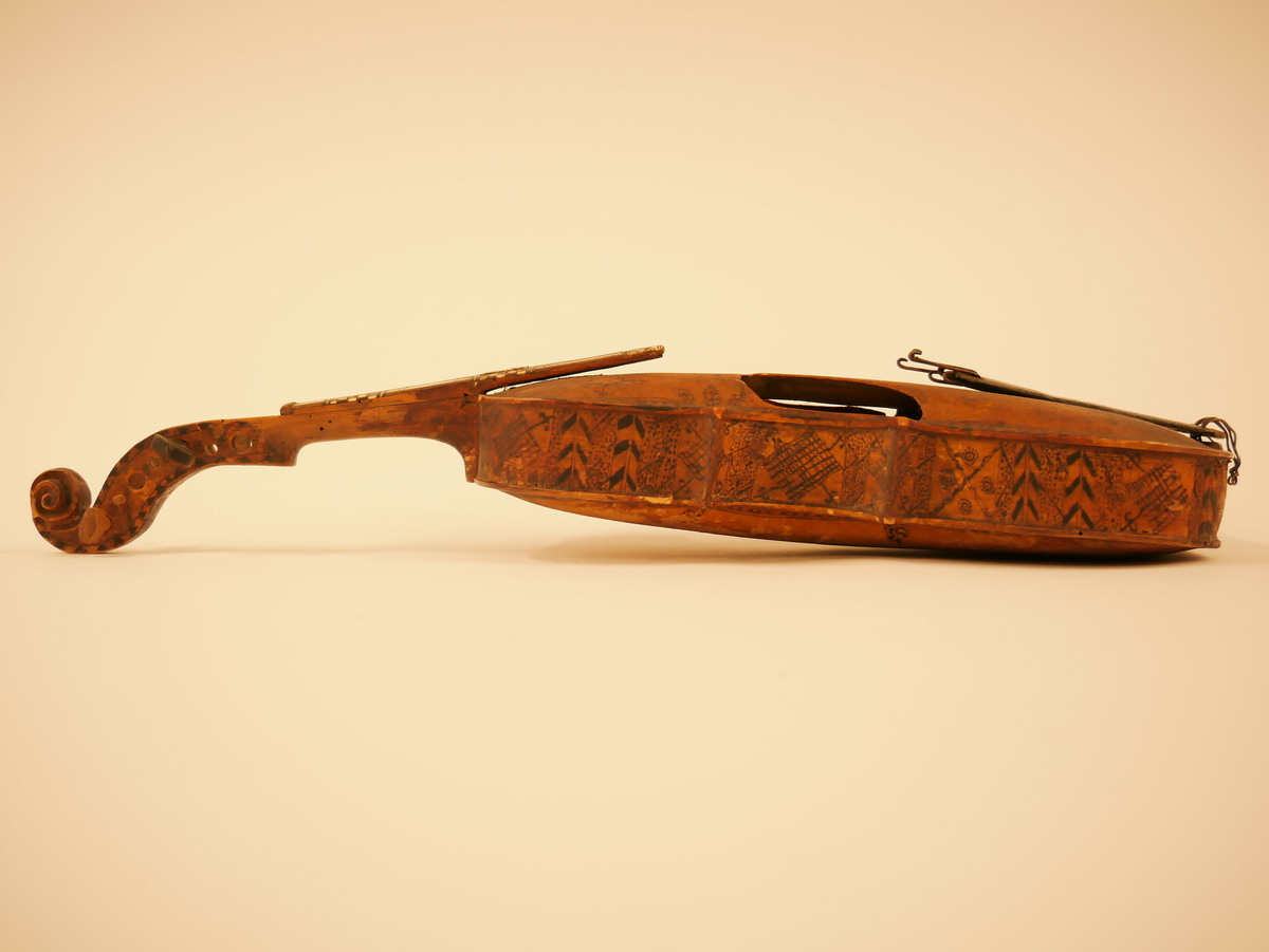 Hardangerfele. Gripebrett med dekor i tre og bein. Rikt dekorert. 
Overflatebehandla med lakk og tusj. Fint avpussa. 
Fela ligg oppi ei felekasse som truleg ikkje høyrar til. 
Lapp med tekst og årstal påskrive limt på innsida av fela.