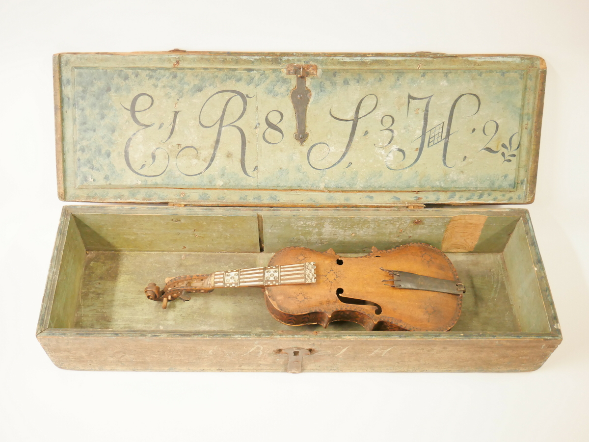 Hardangerfele. Gripebrett med dekor i tre og bein. Rikt dekorert. 
Overflatebehandla med lakk og tusj. Fint avpussa. 
Fela ligg oppi ei felekasse som truleg ikkje høyrar til. 
Lapp med tekst og årstal påskrive limt på innsida av fela.