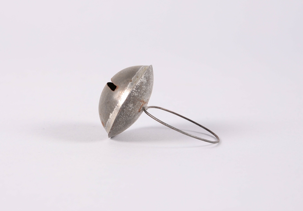 Liten bjelle for husdyr (hund eller katt). Flat dombjelle av metall med smal, rektangulær åpning. En tynn ring er festet til bjellen.

