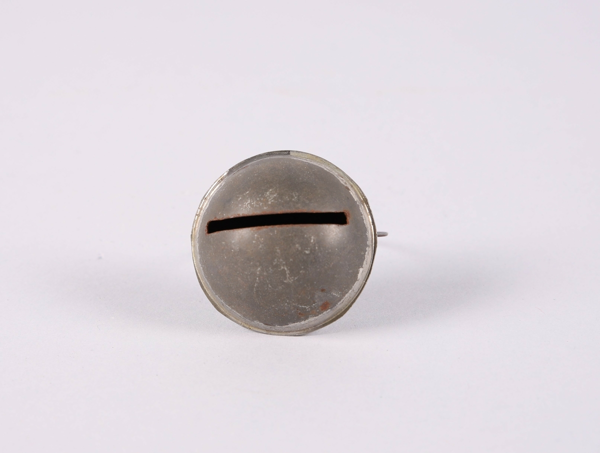 Liten bjelle for husdyr (hund eller katt). Flat dombjelle av metall med smal, rektangulær åpning. En tynn ring er festet til bjellen.

