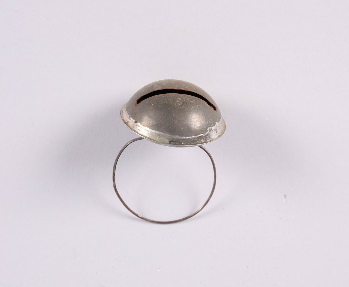 Liten bjelle for husdyr (hund eller katt). Flat dombjelle av metall med smal, rektangulær åpning. En tynn ring er festet til bjellen.


