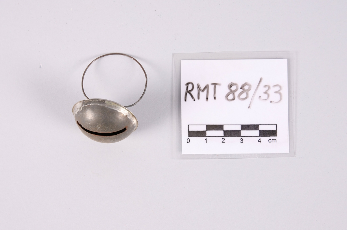 Liten bjelle for husdyr (hund eller katt). Flat dombjelle av metall med smal, rektangulær åpning. En tynn ring er festet til bjellen.

