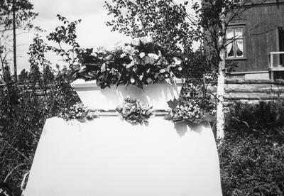 Foto i svart-hvitt av en gravkiste med blomster på. Vedkommende har dødd av spanskesjuken.