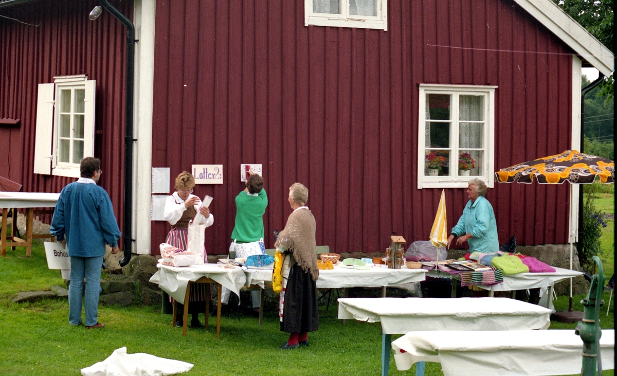 Hembygdsdag på Hembygdsgården Långåker 1:3, cirka 1985 - 1990. Medlemmarna ställer upp lotteri-bord och riggar inför dagens besök. Från vänster: 1. Staffan Bjerrhede (rygg mot kameran), 2. Karin Gustafsson (klädd i hembygdsdräkt), 3. Inga Brandin (i grön tröja), 4. Maj-Britt Andersson och 5. Ingegerd Lundell.