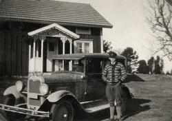 En ung man i plusfours, tröja och skärmmössa står bredvid en