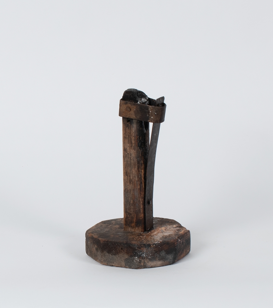 Lysestake av tre. En jernplate er festet langs staken og holder lyset i spenn med en jernring.