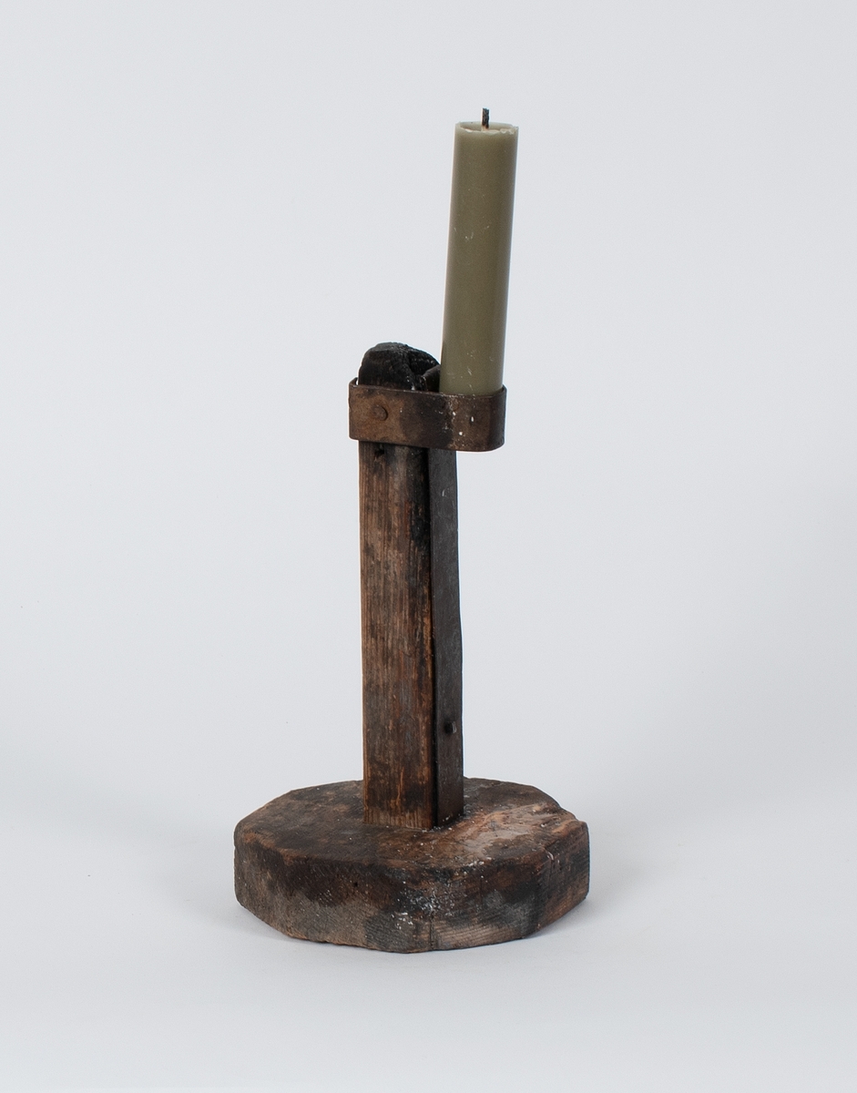 Lysestake av tre. En jernplate er festet langs staken og holder lyset i spenn med en jernring.