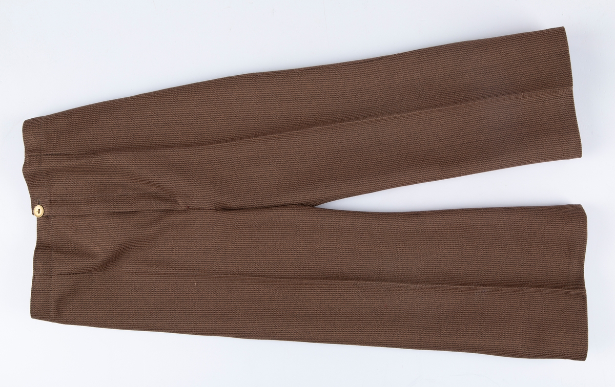 Buksedress. A: Jakke. B: Bukse.

A: Jakke. 
Rund hals, uten krage. 3 par messingknapper, 3 knapphull. Buet lengdesnitt foran og bak. Lange ermer. Falske lommeklaffer i snittsøm foran.

B: Bukse: 
Nedbrettet linning, med strikk på bakstykket. Glidelås i gylf. Buksebena har "sleng". 
Buksen har produksjonsmerke for stoffet