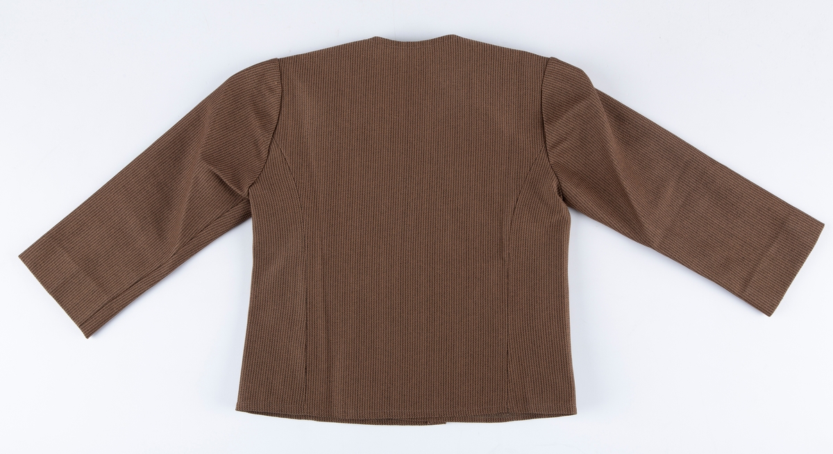 Buksedress. A: Jakke. B: Bukse.

A: Jakke. 
Rund hals, uten krage. 3 par messingknapper, 3 knapphull. Buet lengdesnitt foran og bak. Lange ermer. Falske lommeklaffer i snittsøm foran.

B: Bukse: 
Nedbrettet linning, med strikk på bakstykket. Glidelås i gylf. Buksebena har "sleng". 
Buksen har produksjonsmerke for stoffet