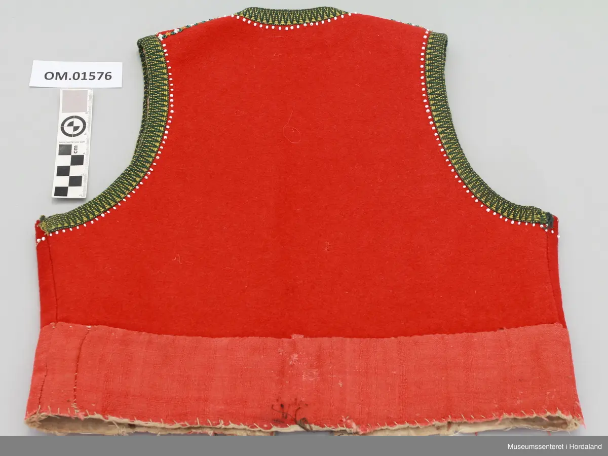 Raudt liv med krokakvarde i gult og grønt. Rad med påsydde kvite enkeltperler innom kvarden. Oppå begge skuldersaumane er det sydd på ei perlebord laga av gule, grøne og kvite perler. Livet er skøytt på i nedre kanten med eit anna stoff (heimevove?) som no har ein falma raudfarge. Livet har forstoff i ubleika bomullsstoff og har to hekter til attlat nede. Handsauma.