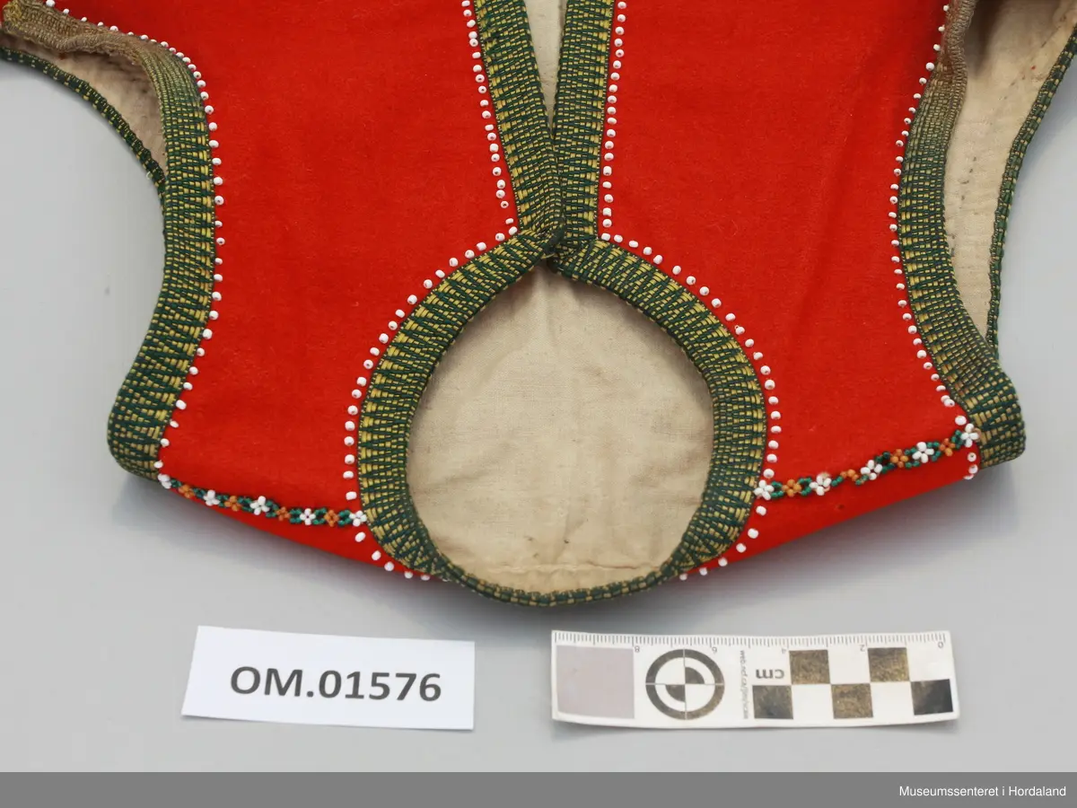 Raudt liv med krokakvarde i gult og grønt. Rad med påsydde kvite enkeltperler innom kvarden. Oppå begge skuldersaumane er det sydd på ei perlebord laga av gule, grøne og kvite perler. Livet er skøytt på i nedre kanten med eit anna stoff (heimevove?) som no har ein falma raudfarge. Livet har forstoff i ubleika bomullsstoff og har to hekter til attlat nede. Handsauma.