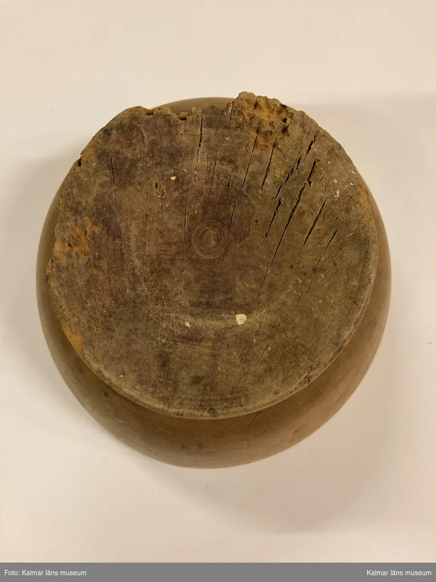 KLM 6153. Ostform. Av trä. Svarvad skål med låg fot. I botten ett snidat mönster i form av en vinkvist med en druvklase.
