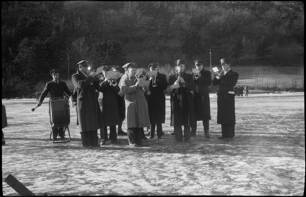 Skøytekonkurransen Dalbumesterskapet. Et korps og mange folk er samlet for å se skøyteløperne.