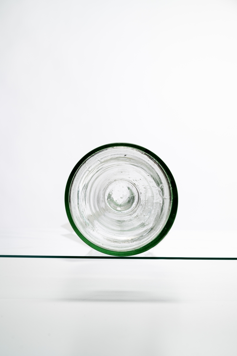 Butelj av ofärgat klart glas, avsedd för tillslutning med naturkork. Buteljen har "Kinnekullebotten". Buteljen tillverkades för klart okryddat brännvin. Klart glas användes för att innehållets äkta färg inte skulle missfärgas av glasets färg (estetisk funktion). Glaset har en drygt 18 cm lång lodrät spricka. Hantverksmässigt tillverkad vid Sunds glasbruk, Jönköpings län. Se vidare Historik.