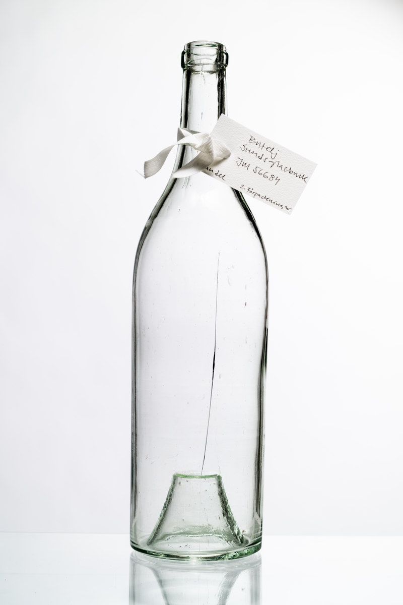 Butelj av ofärgat klart glas, avsedd för tillslutning med naturkork. Buteljen har "Kinnekullebotten". Buteljen tillverkades för klart okryddat brännvin. Klart glas användes för att innehållets äkta färg inte skulle missfärgas av glasets färg (estetisk funktion). Glaset har en drygt 18 cm lång lodrät spricka. Hantverksmässigt tillverkad vid Sunds glasbruk, Jönköpings län. Se vidare Historik.
