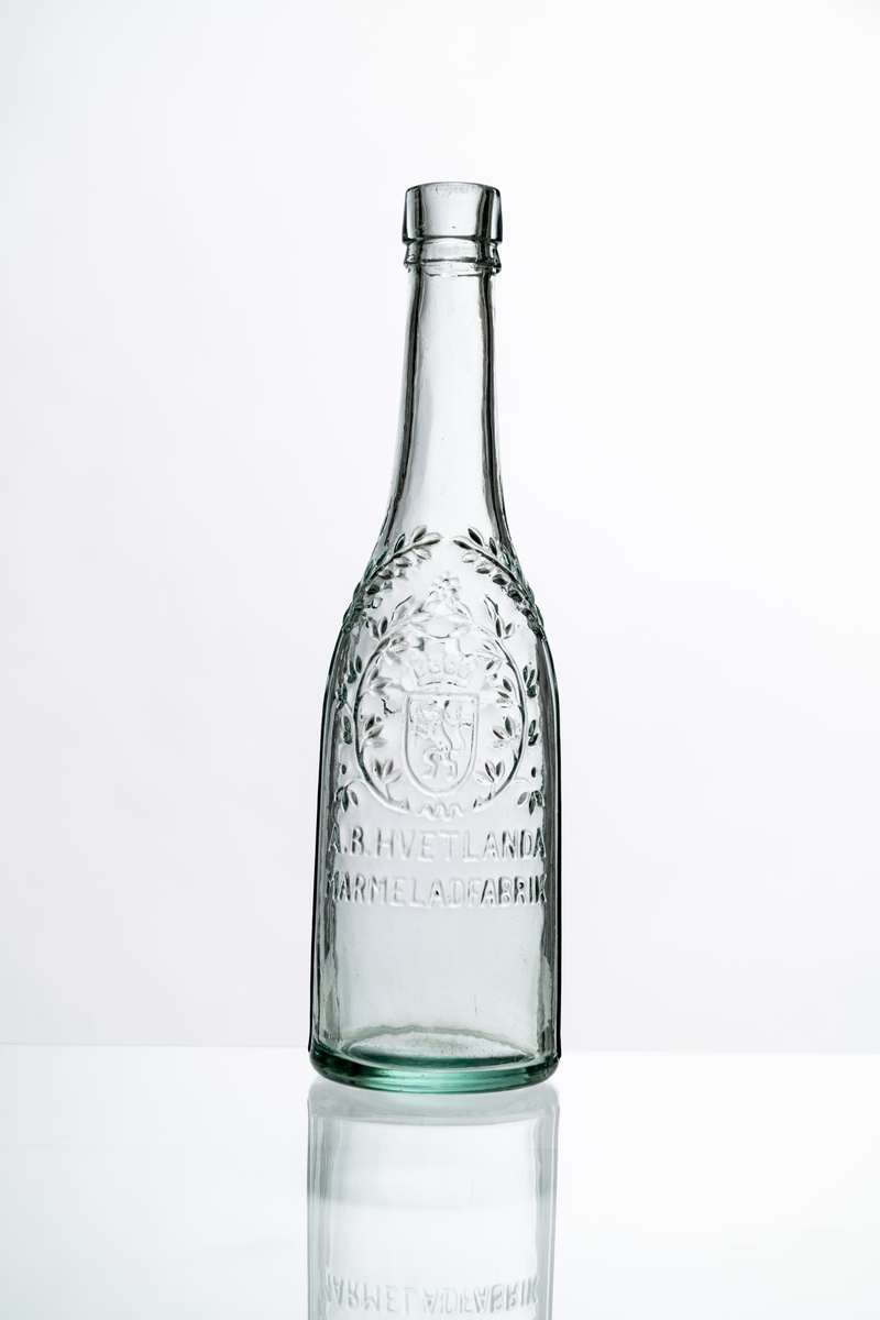 Flaska av ofärgat, klart glas, dekorerad i relief med bladslingor, bär och bild av ett krönt lejon. Märkning i relief på bröstet: "A.B. HVETLANDA MARMELADFABRIK". Tillslutning saknas. Hantverksmässigt tillverkad vid Sunds glasbruk, Jönköpings län. Se vidare Historik.