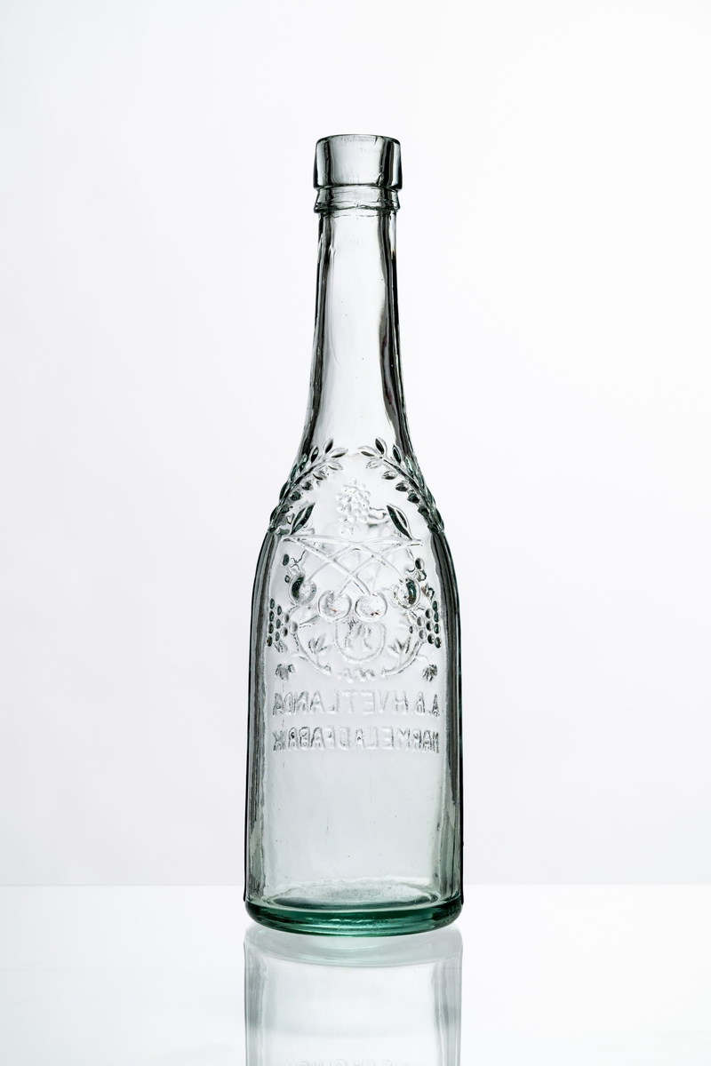Flaska av ofärgat, klart glas, dekorerad i relief med bladslingor, bär och bild av ett krönt lejon. Märkning i relief på bröstet: "A.B. HVETLANDA MARMELADFABRIK". Tillslutning saknas. Hantverksmässigt tillverkad vid Sunds glasbruk, Jönköpings län. Se vidare Historik.
