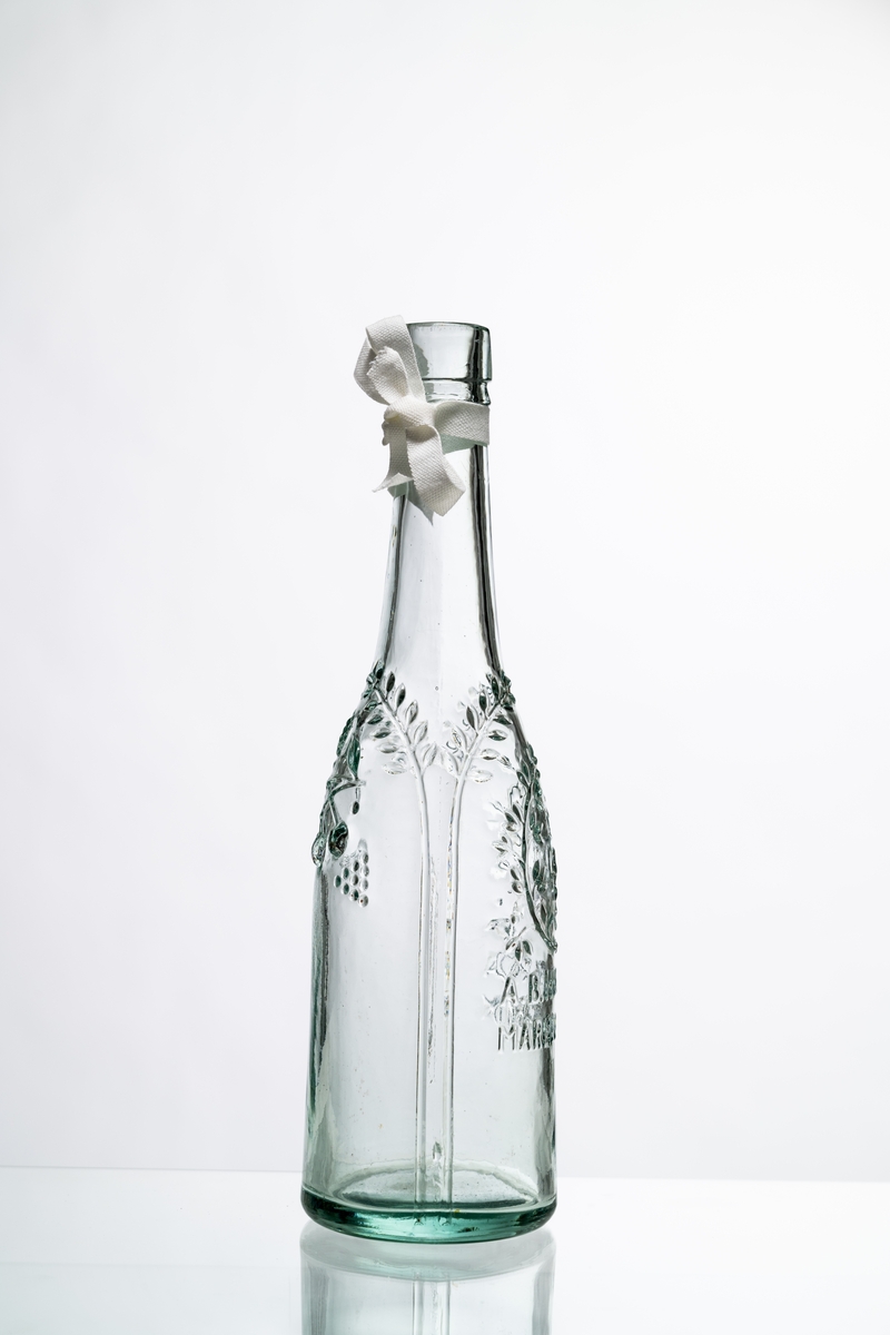 Flaska av ofärgat, klart glas, dekorerad i relief med bladslingor, bär och bild av ett krönt lejon. Märkning i relief på bröstet: "A.B. HVETLANDA MARMELADFABRIK". Tillslutning saknas. Hantverksmässigt tillverkad vid Sunds glasbruk, Jönköpings län. Se vidare Historik.
