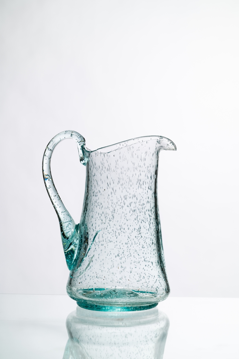 Kanna, den så kallade Kungakannan, av ljust grönfärgat glas. Kannan har rund botten med puntelmärke, insvängd form upp mot mynningen, försedd med grepe och utvikt snip. Spricka i glaset nedanför grepen. Bubblorna i glaset beror på att glasmassan inte kom upp i tillräckligt hög temperatur, för att blåsorna i den tröga massan helt skulle kunna försvinna. Hantverksmässigt tillverkad. Se vidare Historik.