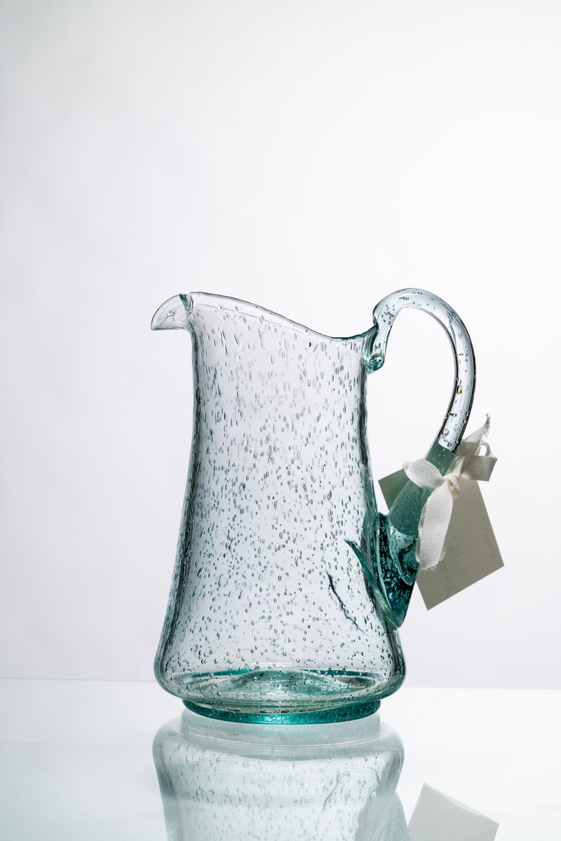 Kanna, den så kallade Kungakannan, av ljust grönfärgat glas. Kannan har rund botten med puntelmärke, insvängd form upp mot mynningen, försedd med grepe och utvikt snip. Spricka i glaset nedanför grepen. Bubblorna i glaset beror på att glasmassan inte kom upp i tillräckligt hög temperatur, för att blåsorna i den tröga massan helt skulle kunna försvinna. Hantverksmässigt tillverkad. Se vidare Historik.