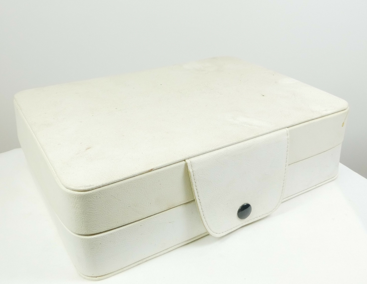 Hvit rektangulær boks med lokk. Inneholder et massasjeapparat. 