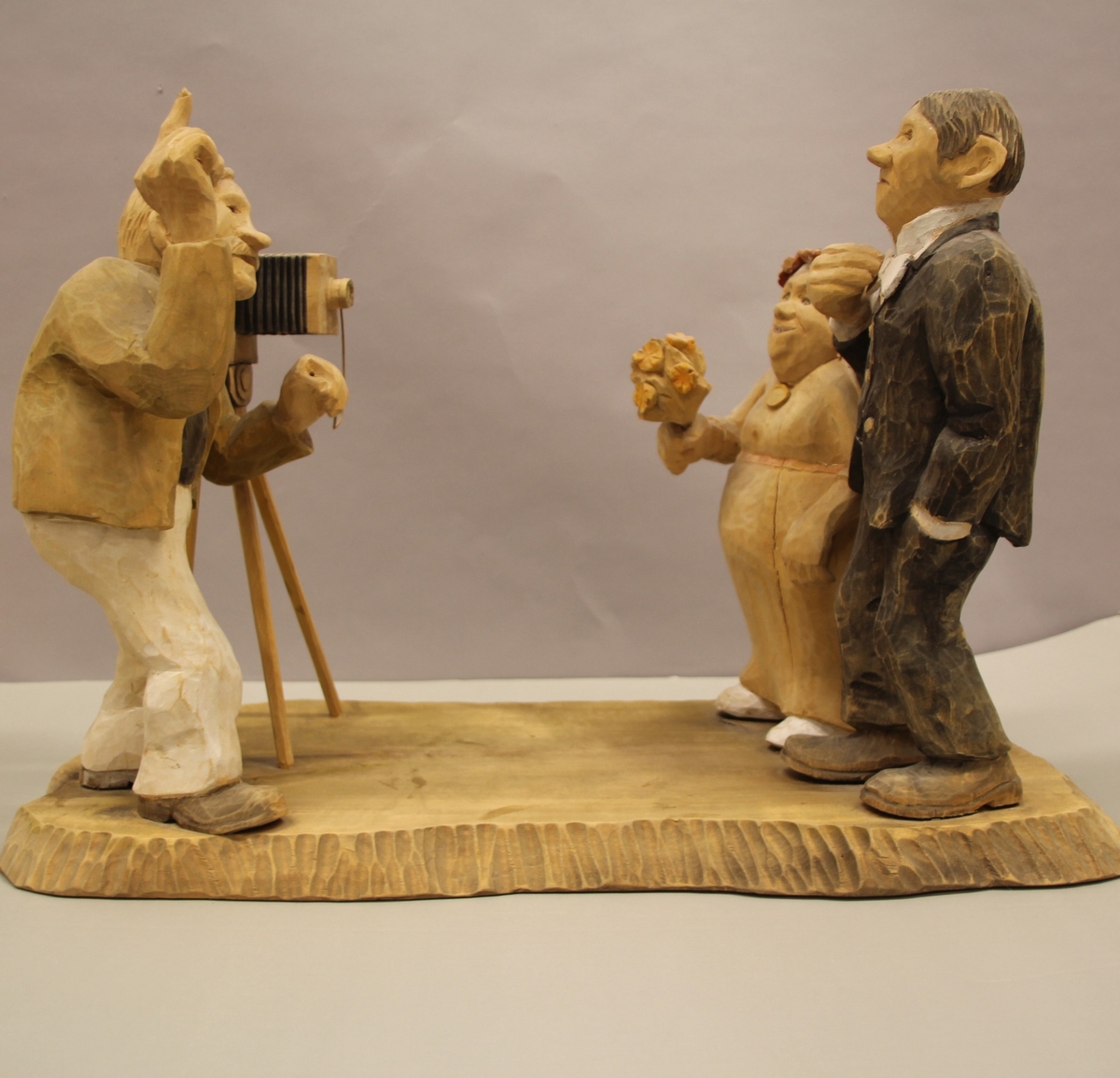 Skulptur som syner Arne Aas som tek bilete av eit brudepar. Skulpturen er skoren i tre.Tekst under:"Bjarne Walle fra Bamle laget denne gruppa på bestilling i fra fotografen Arne Aas i 1984" "Motiv: Arne Aas fotograferer brudepar". Bokstavane BW skore inn under skulpturen.